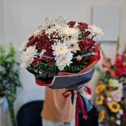 White and maroon chrysanthemums with baby’s breath arranged in a round bouquet with green leaves