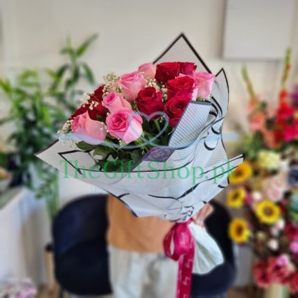 A bouquet of pink and red roses with baby’s breath wrapped in a white paper and tied with a red ribbon.