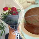 Blossom and Bite: A person holding a beautiful flower arrangement of red, white and yellow mix flowers wrapped in black paper with a white ribbon. Next to them, a chocolate cake with a smooth chocolate frosting and the words “Chocolate Heaven” written on the top right corner on a white plate.