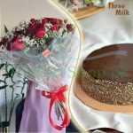 Three Milk Rose: A photo of a three milk cake and a bouquet of red roses on a table. The cake is round and has a smooth chocolate frosting and gold sprinkles on the sides. The roses are red and wrapped in a clear plastic with a red ribbon and a card that reads “love”. The text “Three Milk” and “GiftShop.pk” are visible in the top right corner of the photo.