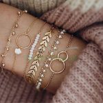 A set of five gold charm bracelets on a person’s wrist, featuring white beads and gold leaf and circle charms. 🌟