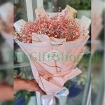 A photo of a bouquet of pink baby’s breath flowers wrapped in white paper and tied with a pink ribbon