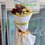 A bouquet of red, white, and pink imported flowers wrapped in white paper and tied with a gold ribbon.