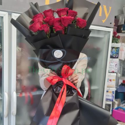 Radiant Romance: A person holding a bouquet of 12 imported red roses wrapped in dark paper and red ribbon
