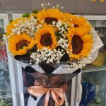 Sunny Gypset: Seven vibrant sunflowers with delicate white gypsophila, wrapped in stylish black and white paper with a peach ribbon.